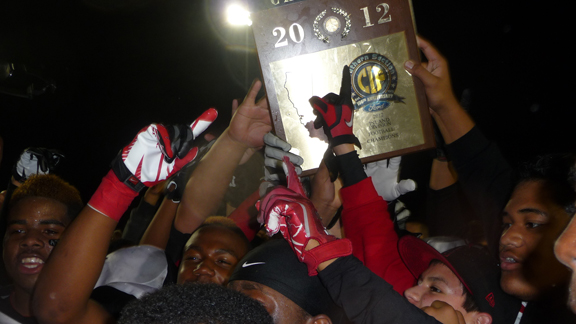 Corona Centennial players swarm around the CIFSS Inland Division championship plaque, hoping to touch it after their team defeated nationally ranked Vista Murrieta 30-28 in game played Nov. 30 at Vista Murrieta.